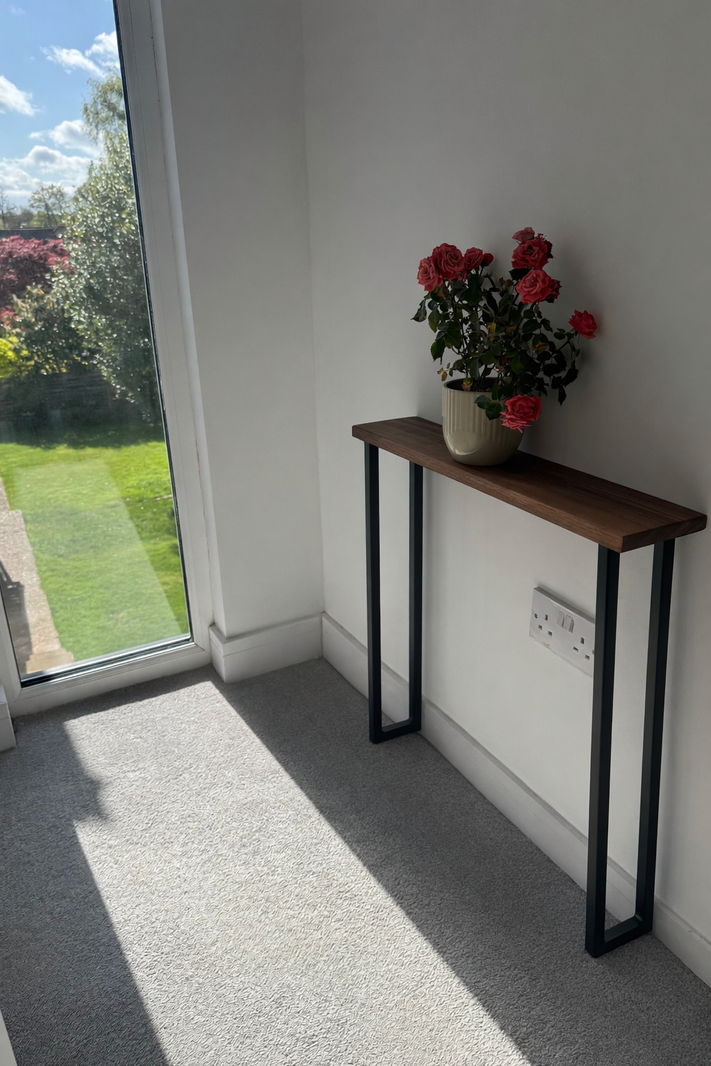 Small wooden table with a potted plant by a window with a view of greenery.