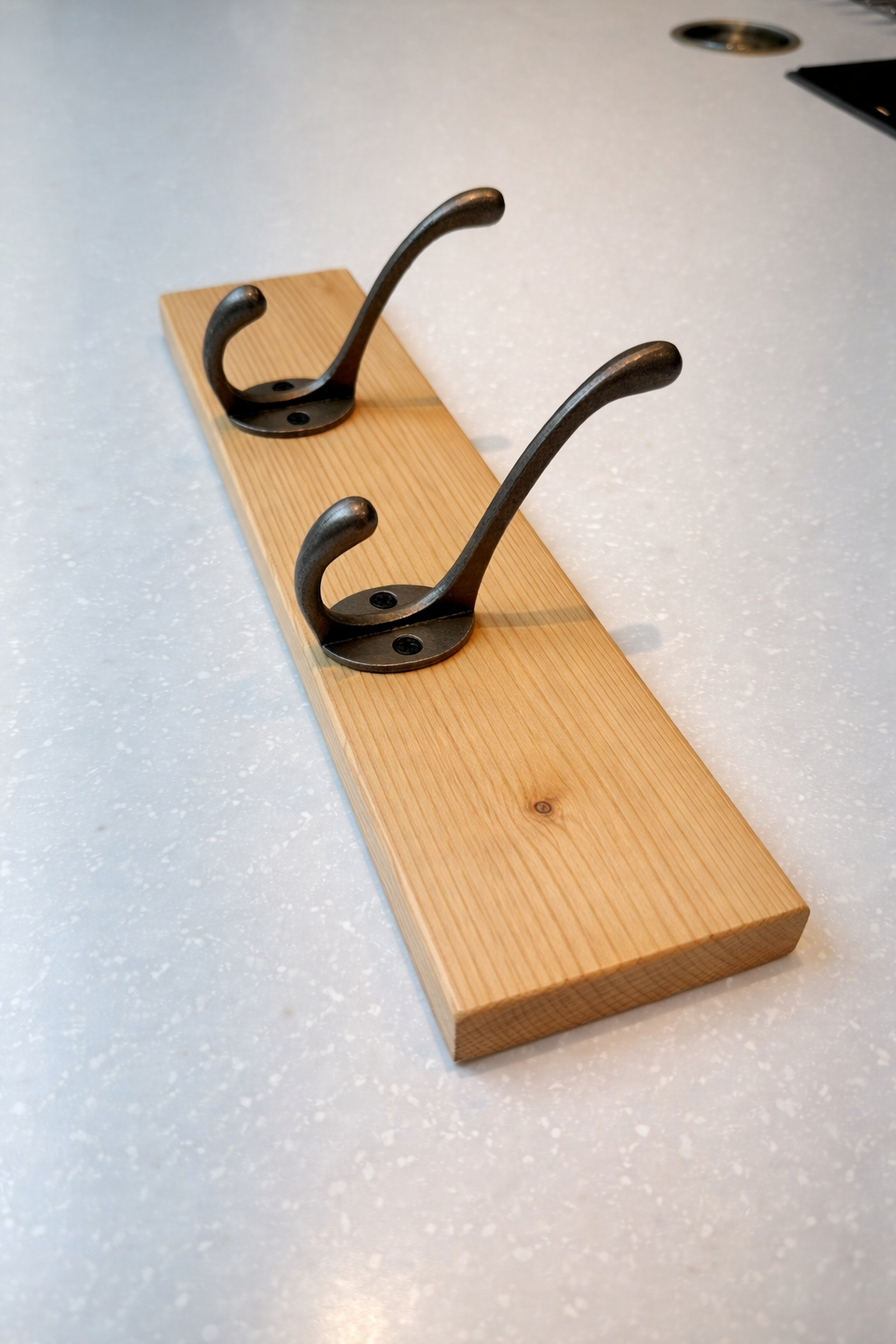 Wooden board with three metal hooks on a light-colored countertop.
